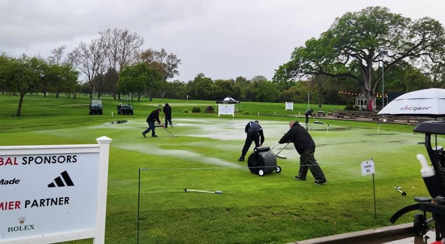 Groundskeepers sweeping and rolling rain off of the putting green