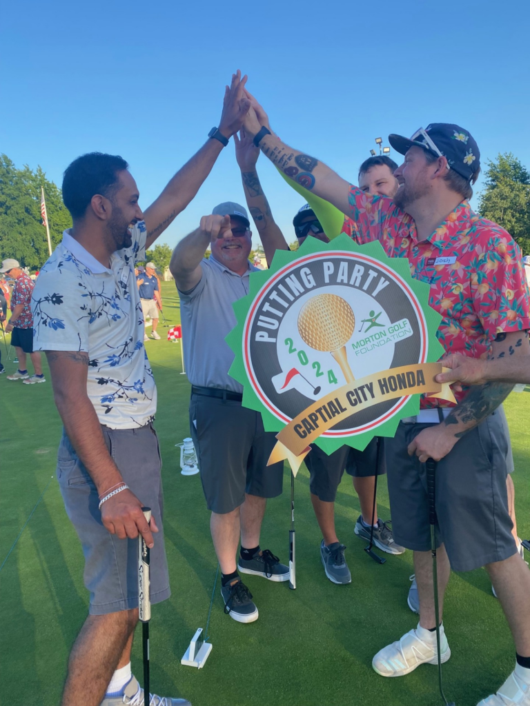 Four golfers high fiving on the putting green
